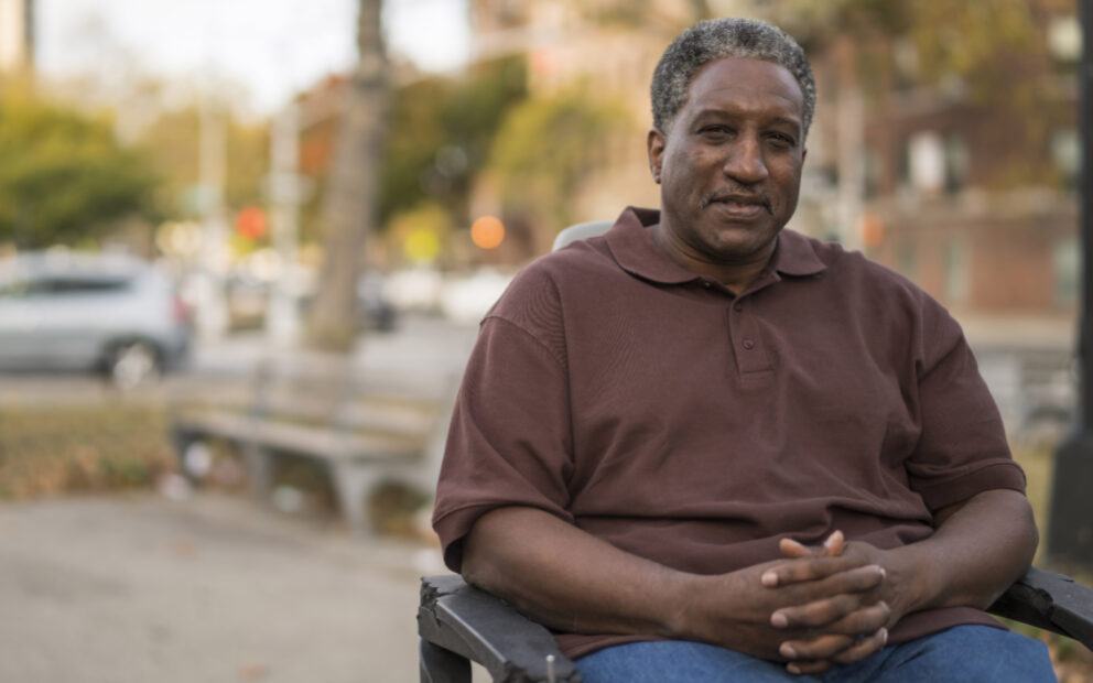 African American man in wheelchair, arms folded, faint smile.