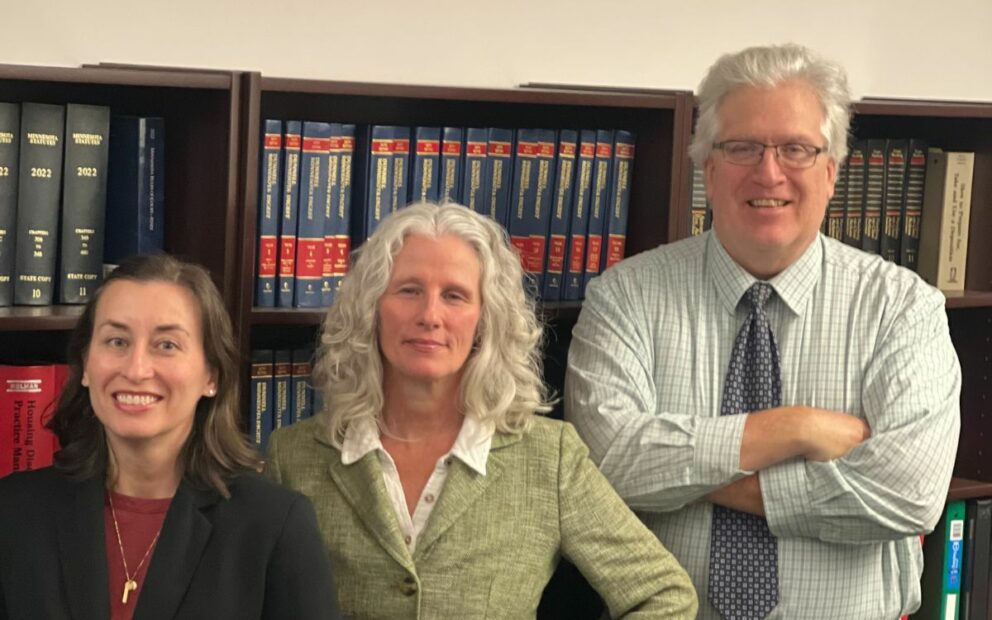 Three staff attorneys stand in front of legal bookcase.