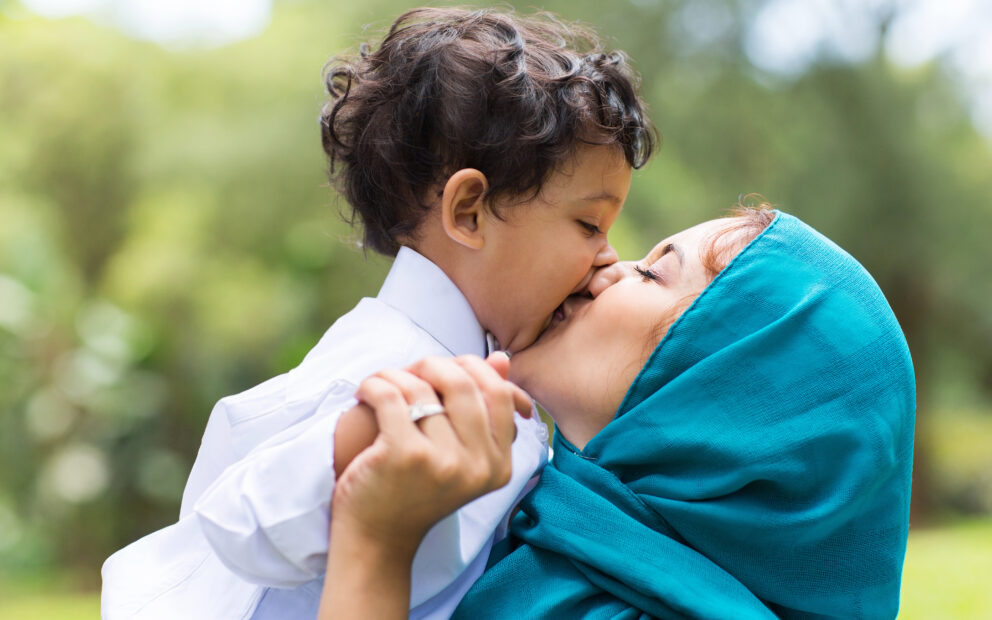 Mother wearing a hijab holds toddler son to her face.