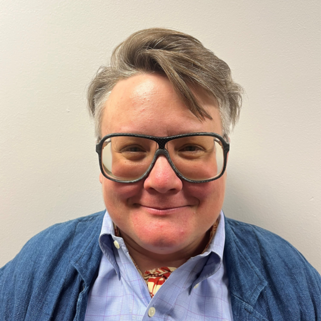 Person smiling, wearing glasses and blue sweater