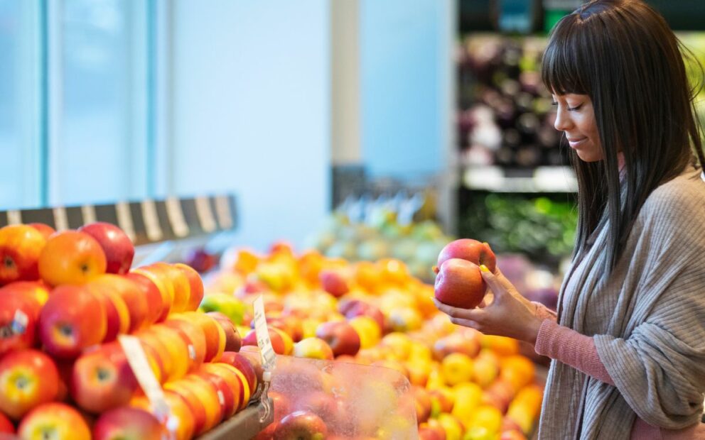 Grocery shopper inspects apples in produce aisle.