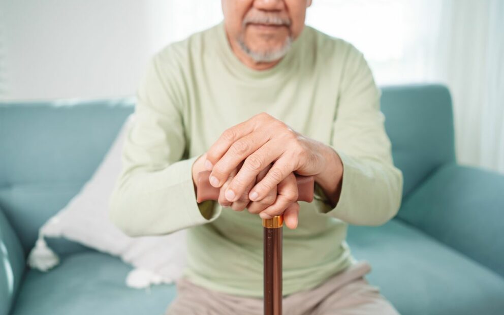 Man in long-sleeve shirt, sitting on a sofa with hands resting on his cane.