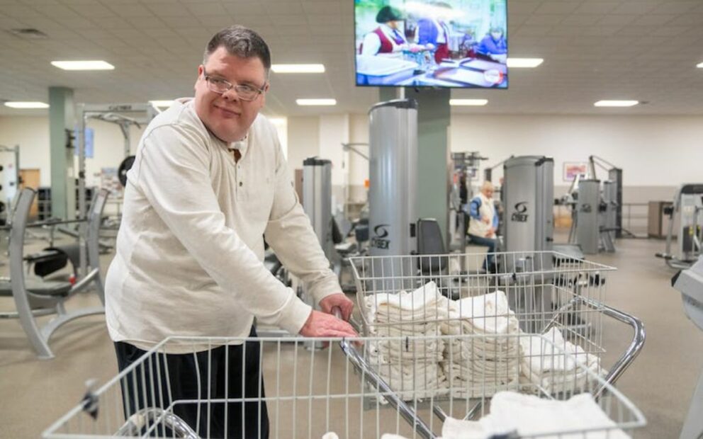 Worker in laundry-folding facility pushes cart.
