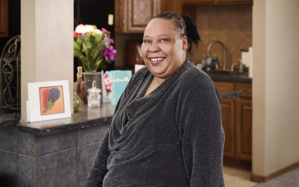 African American woman smiles for camera, kitchen in background.