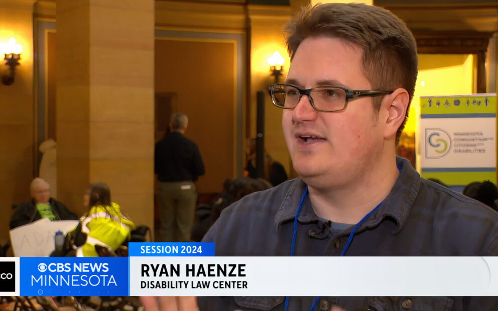 Man in glasses pictured in television interview. Name, Ryan Haenze, Disability Law Center is superimposed at bottom of screen.