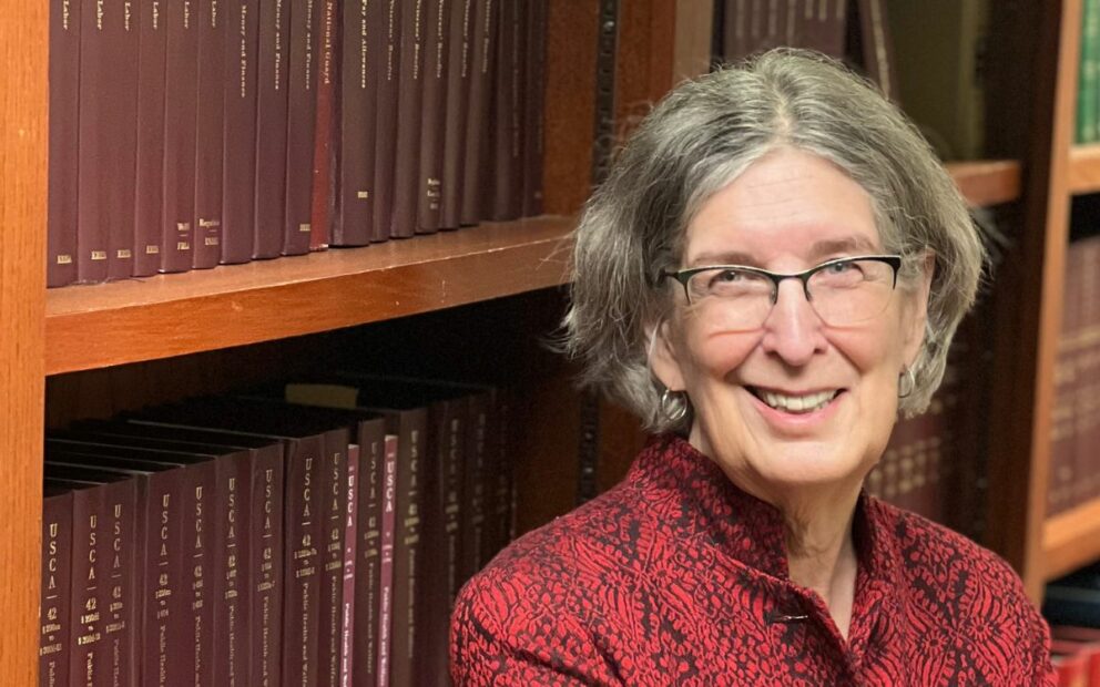 Woman smiles, backdrop is a bookcase of legal texts.