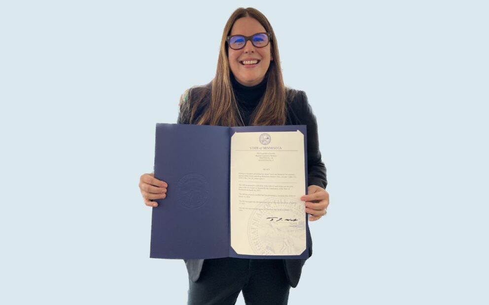 Woman smiles, holding up official state seal document.