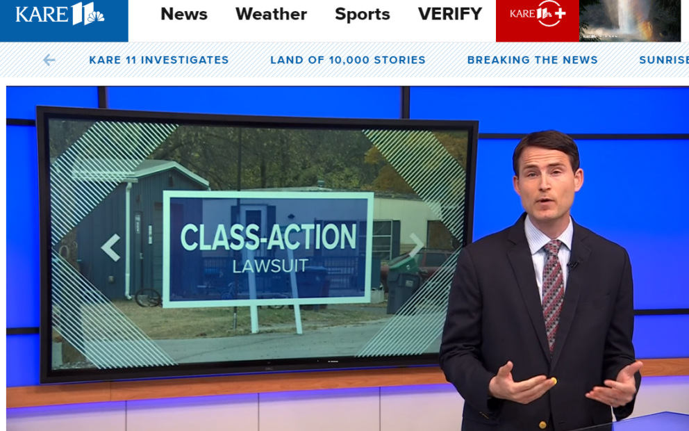 Reporter on news set next to large monitor showing image of Mobile home park with words Class Action superimposed