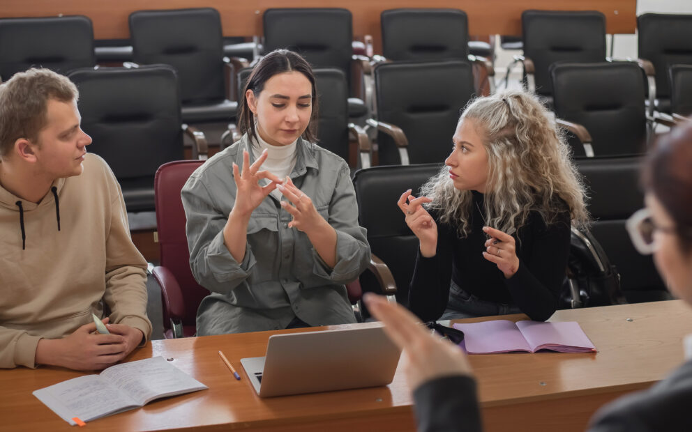 Four individuals use American Sign Language in conversation as they sit at a table.