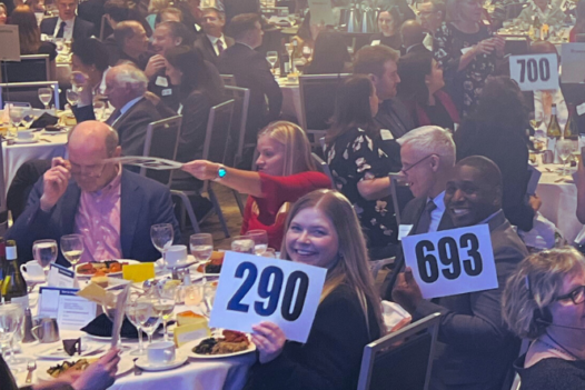 Banquet hall of dinner guests holding up auction placards