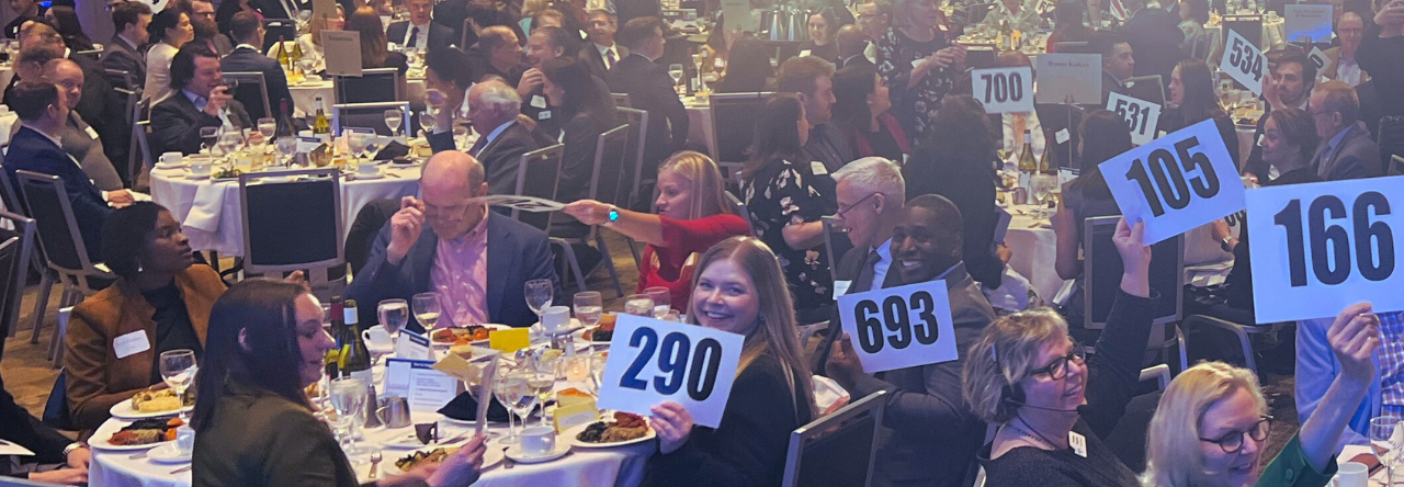 Banquet hall of dinner guests holding up auction placards
