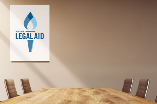 Conference table with six leather backed chairs and a framed poster-size Legal Aid logo on the back wall to the left