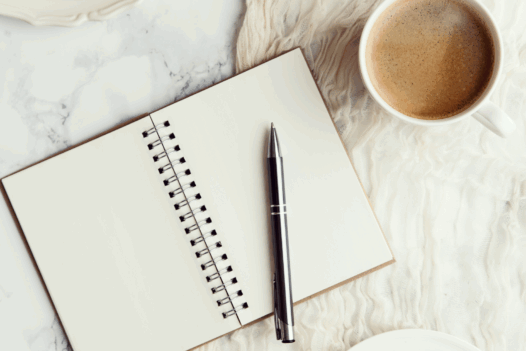 journal with pen and cup of coffee next to it