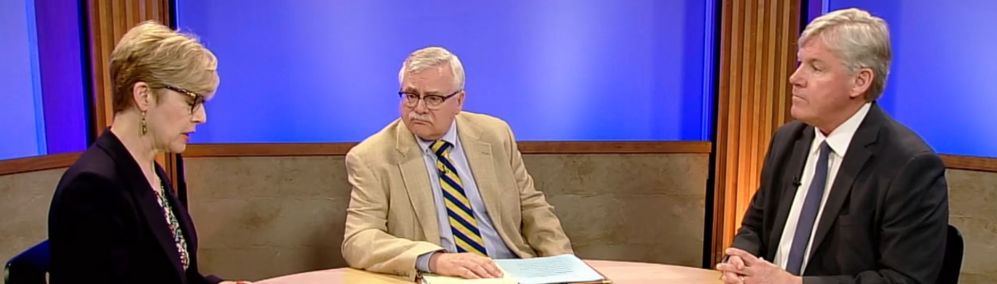 a man and woman sitting at a table interviewing a man on the news