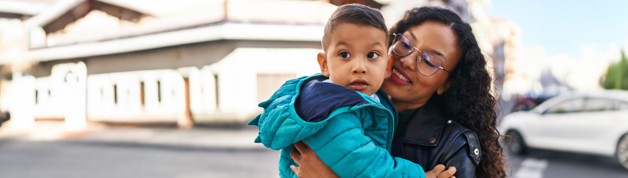 woman holding a child in a blue jacket, in front of a house