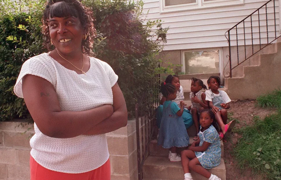 woman standing with arms crossed, with children sitting on stairs