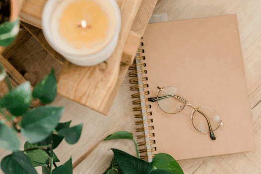 glasses on top of a notebook, with a candle and plant beside it