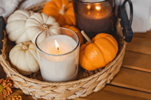 lit candle in a basket with mini white and orange pumpkins