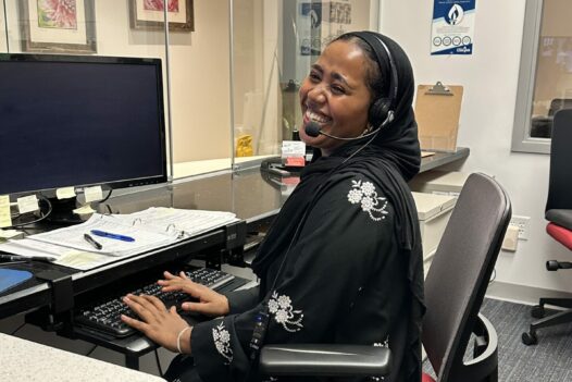 woman wearing headset, sitting at a computer, smiling