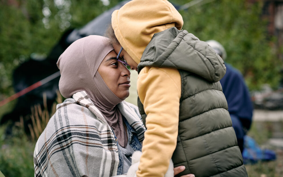iddle-eastern mother in headscarf touching foreheads with daughter while finding her after escape from battlefield