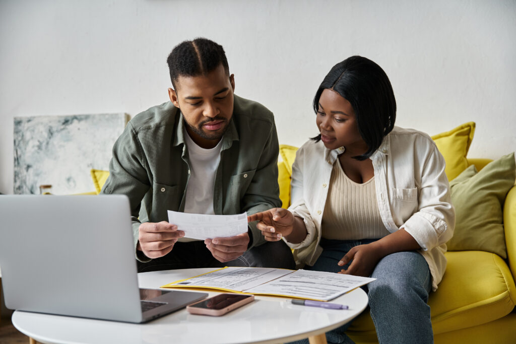 A couple sits at a table in their home, looking over documents together.