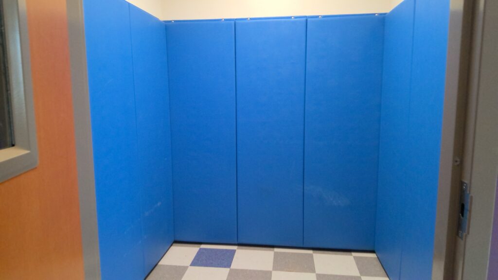 A room with blue padded walls and uncarpeted white and gray checkered floors.
