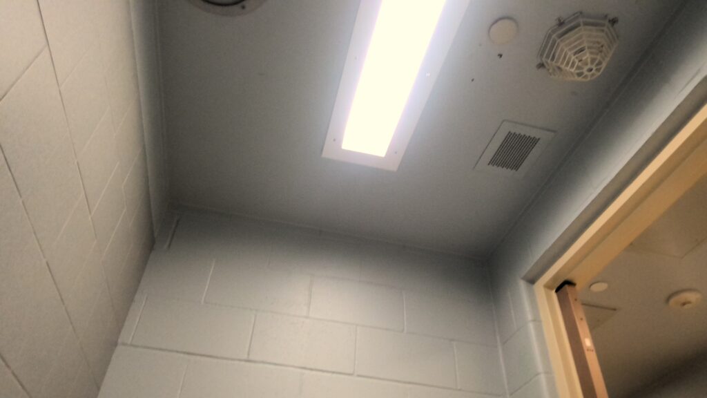 A ceiling and cinder block walls. A grated smoke alarm, ceiling vent, and rectangular recessed lighting are on the ceiling.