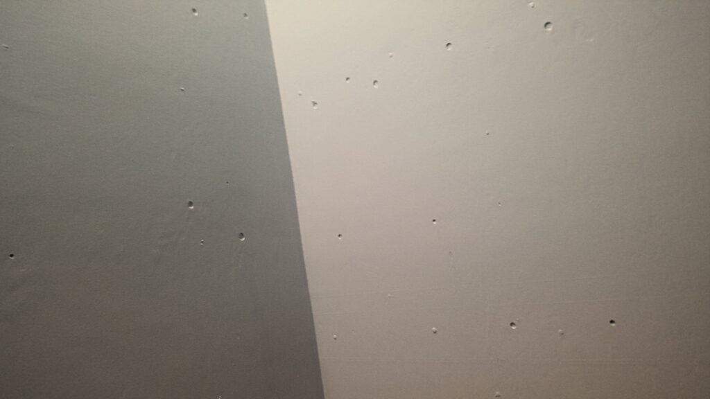 A corner joining two white plaster walls with approximately 15 small holes and indents.