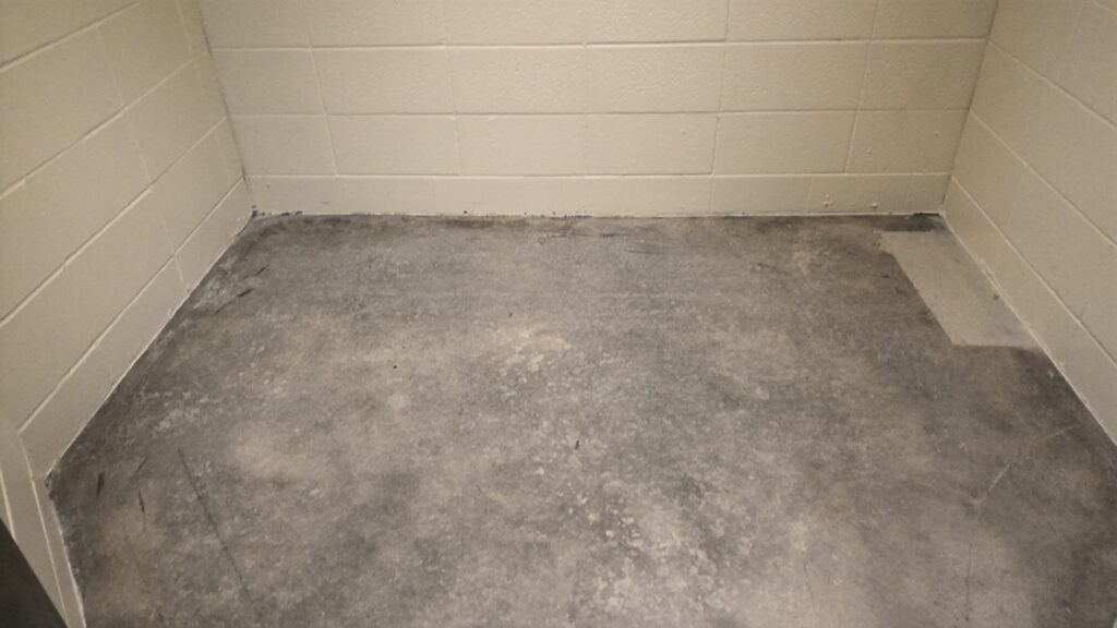 A small room with white cinder block walls and an unfinished cement floor.
