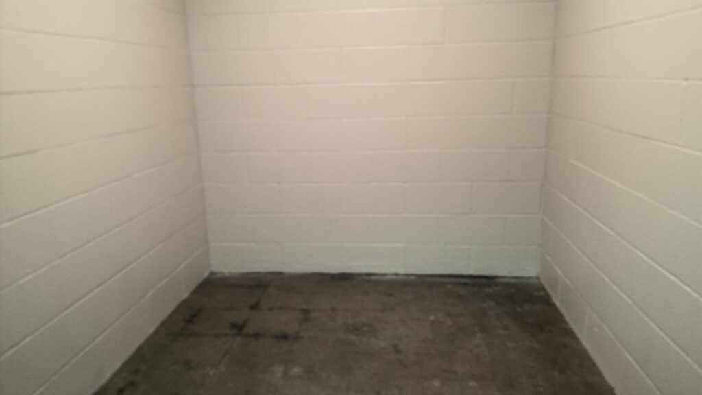 A room with white cinder block walls and discolored concrete flooring.