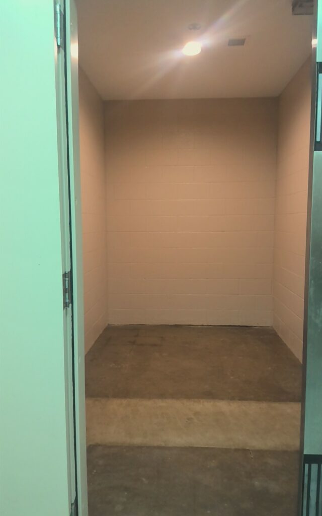 Room with white cinder block walls and discolored concrete floor, viewed through open doorway.
