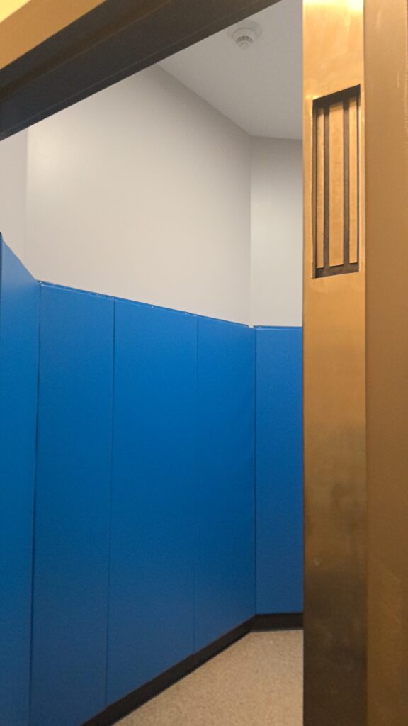 Doorway into room with blue padded walls. Metal strip along edge of doorway.