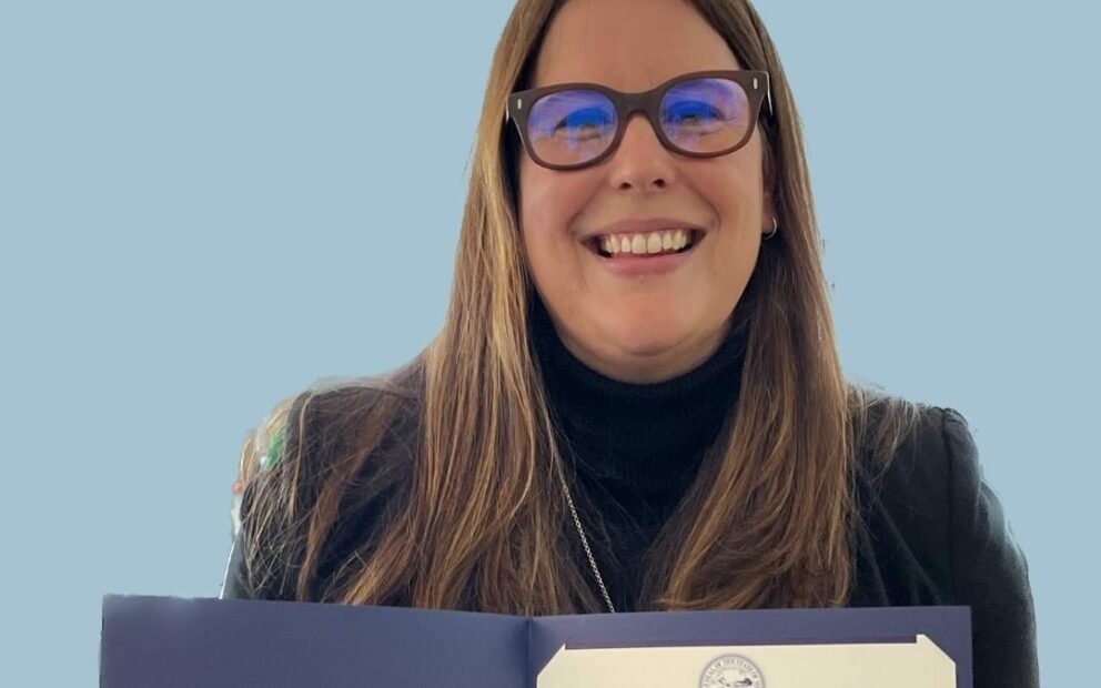 Smiling woman in glasses holds certificate in bound folder