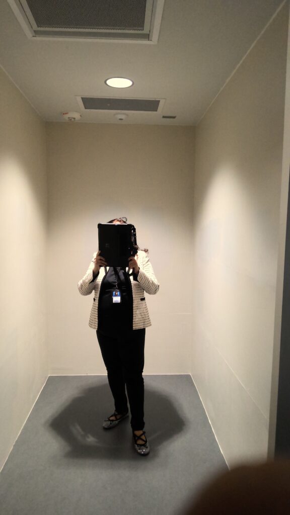 An adult stands in a small room with beige walls and gray flooring.