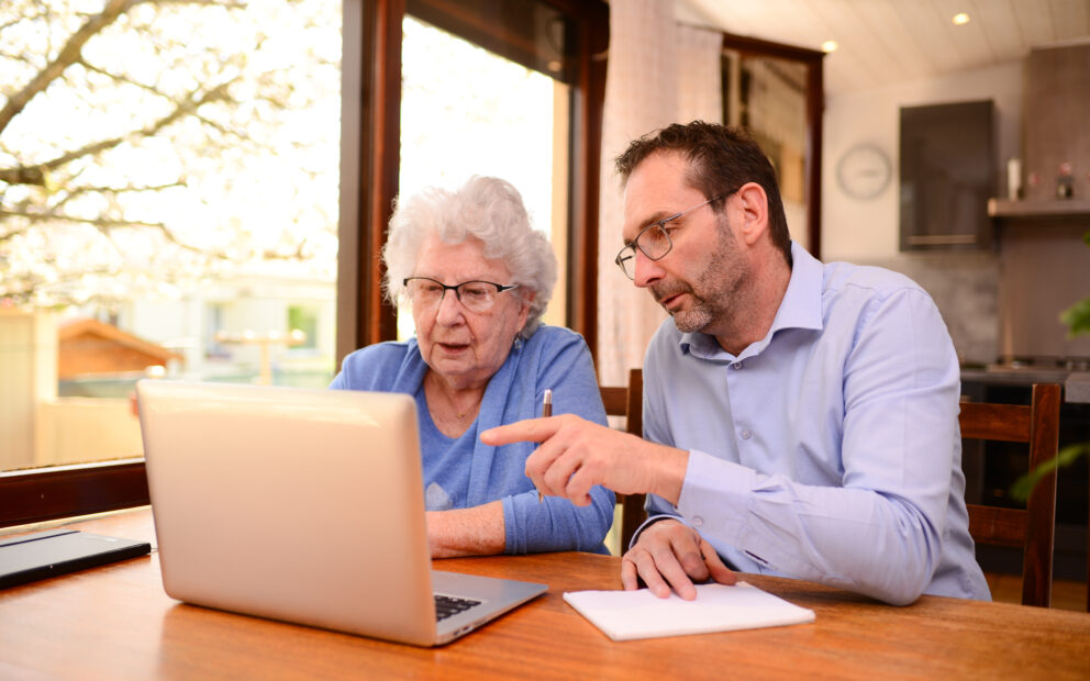 mature man helping elderly senior woman at home with paperwork and computer internet