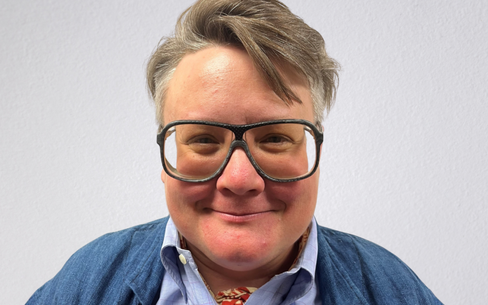 Person smiling, wearing glasses and blue sweater