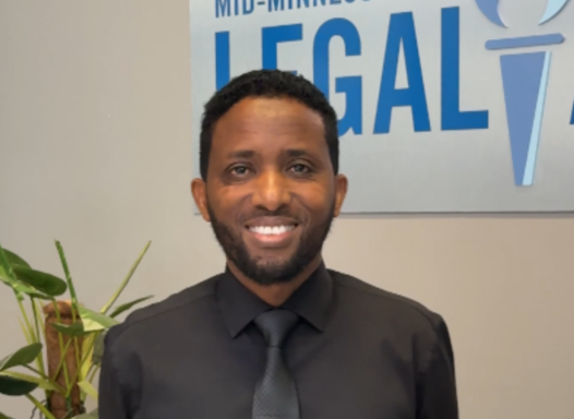 man smiling, standing in front of legal aid logo