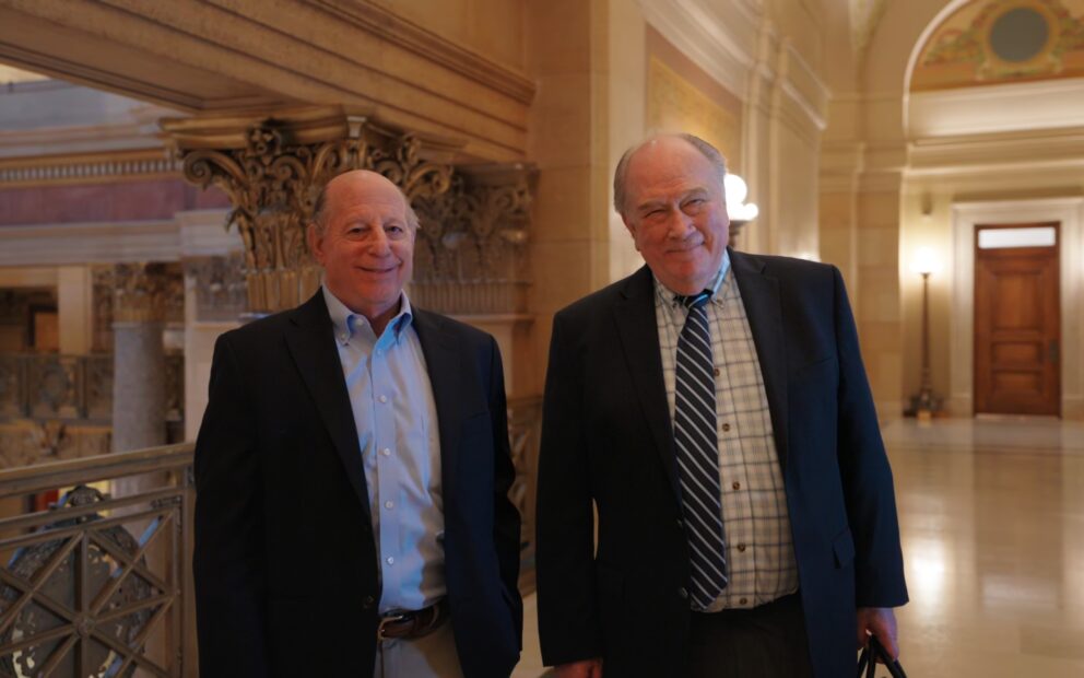 two men wearing suits stand in a government building