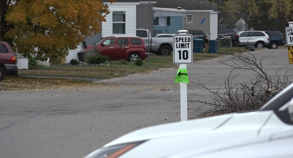Street view of mobile homes with cars parked and a 10 miles per hour sign in the foreground