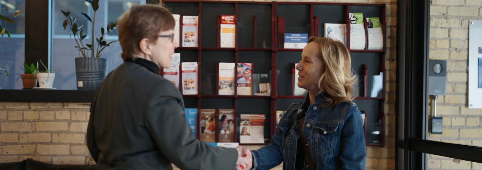 Woman enters lobby door extends hand to another who is also extending a hand as they meet.
